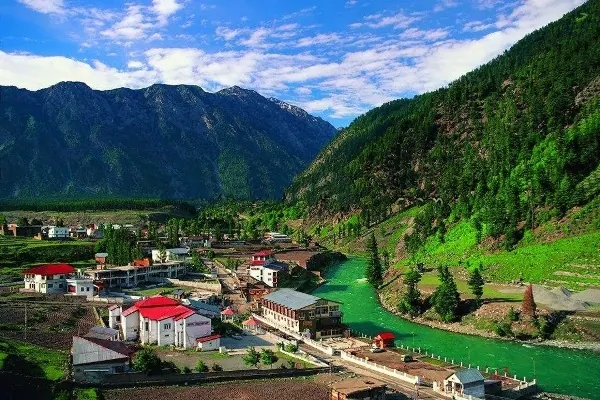 Red-roofed hotels beside a green river in a hill valley of northern Pakistan