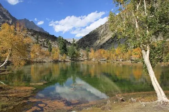 Calm lake reflecting autumn trees and mountains in Naltar valley